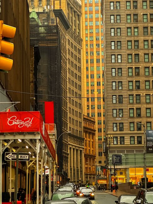 A city street scene featuring tall, historic buildings with brick and stone facades, and modern glass-fronted retail stores at ground level, including a Gap store illuminated with warm lighting. The s